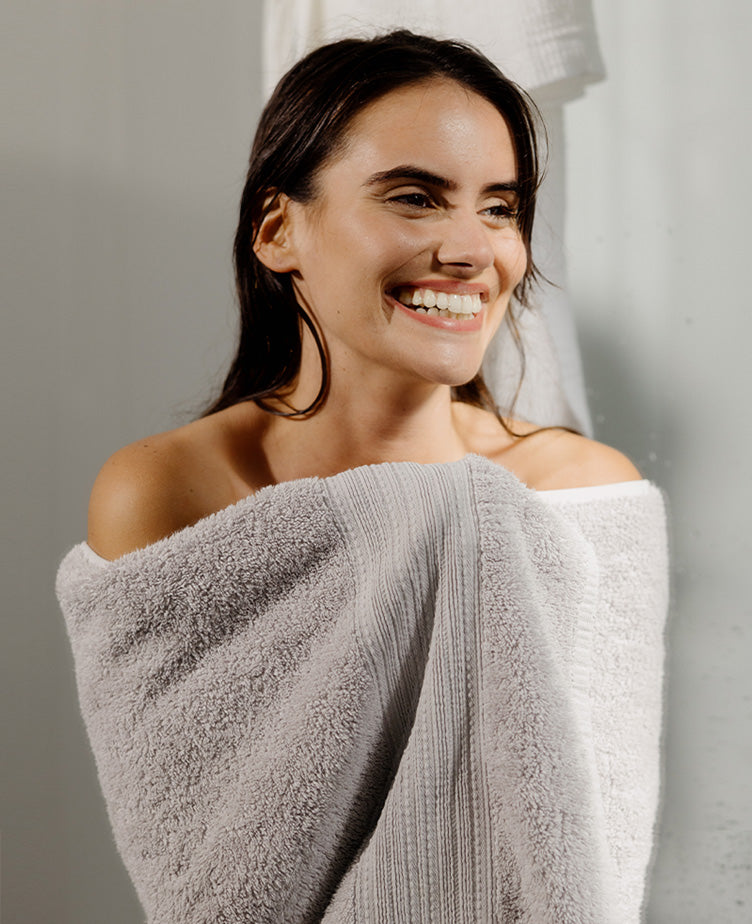 Woman wrapped in a gray towel, smiling against a neutral background